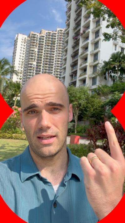 Man wearing blue shirt pointing to buildings behind him.