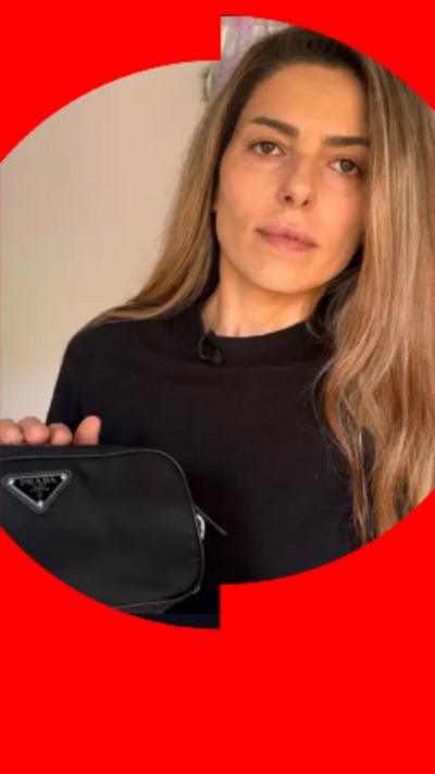 A woman with long blonde hair wearing a black top, holding a black bag.